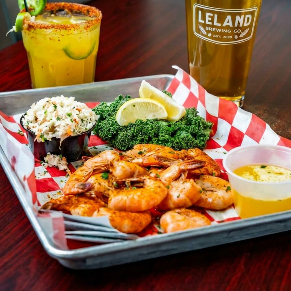 Tray of seasoned shrimp with coleslaw, kale, lemon wedges, dipping sauce, a yellow cocktail, and Leland Brewing Co. beer